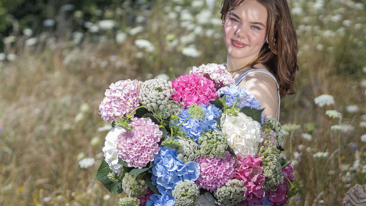 Blumen-Risse, Aktuelles, Hortensien-in-der-Floristik, junge-Frau-steht-mit-romantischem-Hortensienstrauss-auf-Wildwiese
