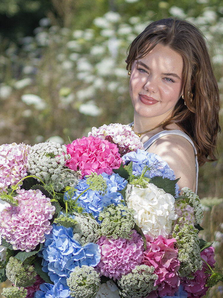 Blumen-Risse, Aktuelles, Hortensien-in-der-Floristik, junge-Frau-steht-mit-romantischem-Hortensienstrauss-auf-Wildwiese