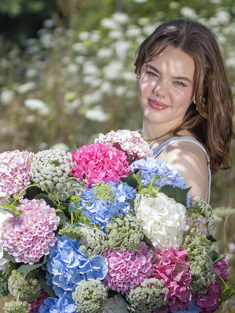 Blumen-Risse, Aktuelles, Hortensien-in-der-Floristik, junge-Frau-steht-mit-romantischem-Hortensienstrauss-auf-Wildwiese
