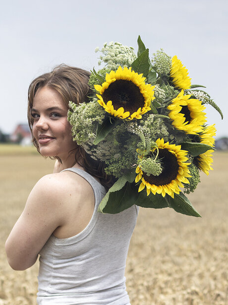 Blumen-Risse, Aktuelles, Aktion-Sonnenblumen, Frau-mit-Sonnenblumen-ueber-Schulter-steht-im-Feld