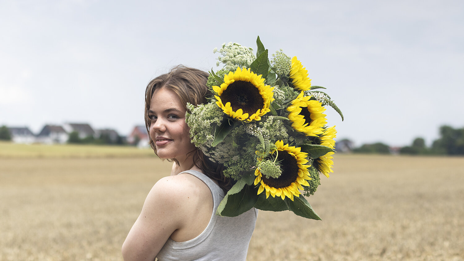 Blumen-Risse, Aktuelles, Aktion-Sonnenblumen, Frau-mit-Sonnenblumen-ueber-Schulter-steht-im-Feld