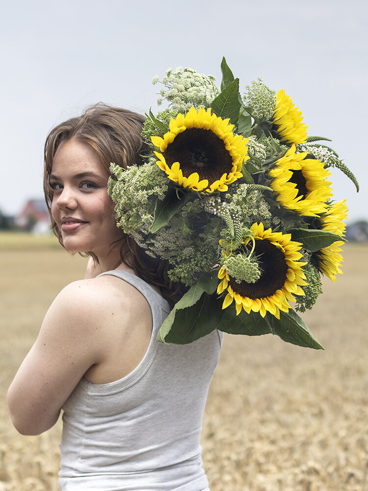 Blumen-Risse, Aktuelles, Aktion-Sonnenblumen, Frau-mit-Sonnenblumen-ueber-Schulter-steht-im-Feld