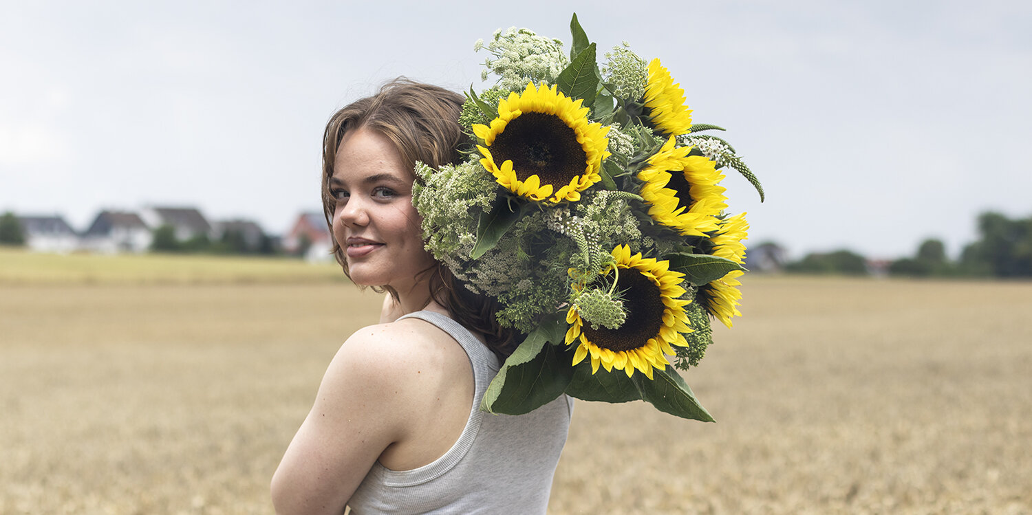 Blumen-Risse, Aktuelles, Aktion-Sonnenblumen, Frau-mit-Sonnenblumen-ueber-Schulter-steht-im-Feld