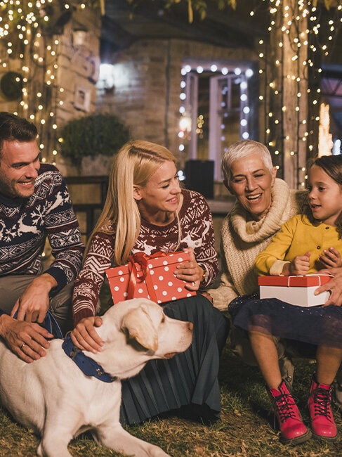 Blumen-Risse, Aktuelles, Vor-Ort-News, Weihnachten, Familie-mit-Hund-und-Geschenken-vor-Weihnachtlich-beleuchtetem-Haus