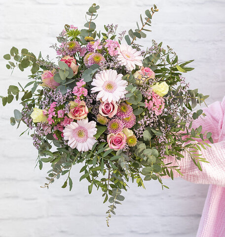 Blumen-Risse, Blumenversand, SW002-Hauptsache-Pink, Rosa, Pink, Frau-haelt-rosafarbenen-Blumenstrauss-mit-zwei-Haenden-vor-weisser-Steinwand