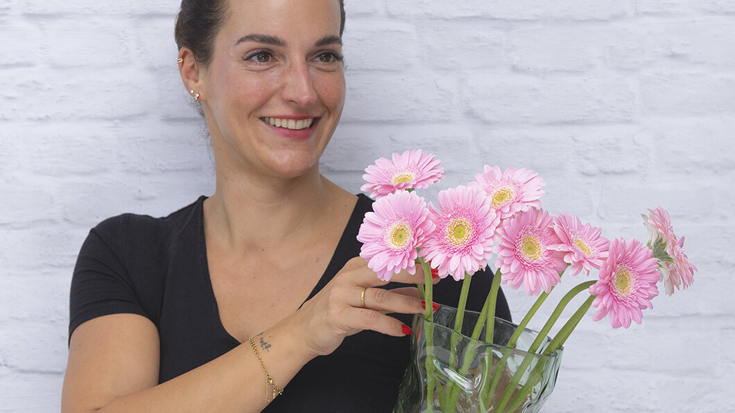 Blumen-Risse, Schnittblumen, SB007-Blumenbox-Mini-Gerbera, Rosa-15-Stueck, Rosa, Frau-haelt-gruene-Vase-mit-Mini-Gerbera-auf-linker-Huefte