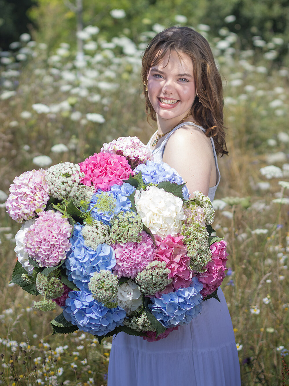 Blumen-Risse, Aktuelles, Hortensien-in-der-Floristik, junge-Frau-steht-mit-grossem-Hortensienstrauss-auf-Wildwiese