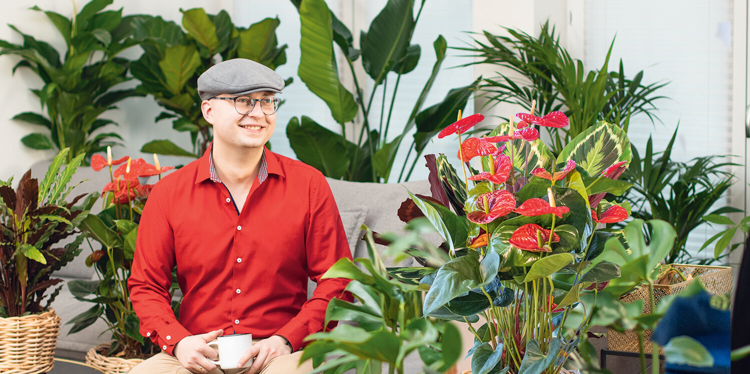 Ratgeber, Zimmerpflanzen, Gruenpflanzen, sitzender-Mann-zwischen-vielen-Gruenpflanzen-in-Wohnzimmer